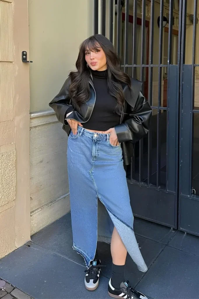 Spring Outfit Ideas with a black fitted turtleneck, asymmetrical denim midi skirt, and a leather jacket, paired with sneakers and soft waves.