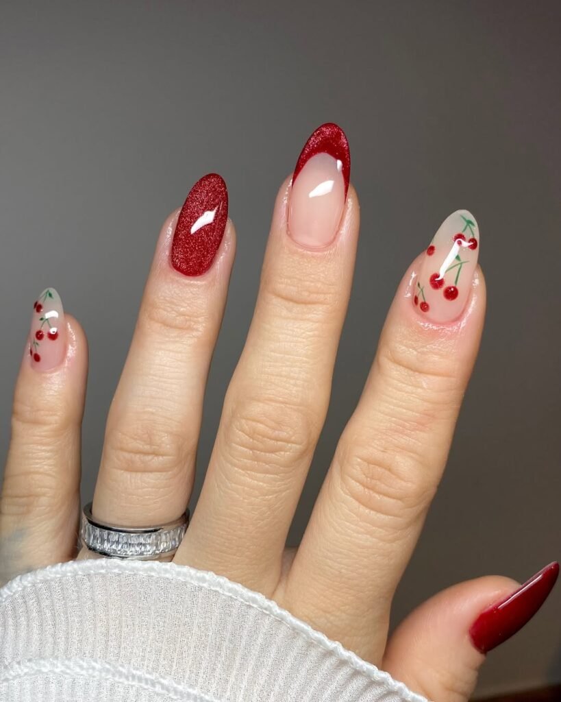 Almond nails with glittery red polish, red French tips, and cherry nail art on nude bases.