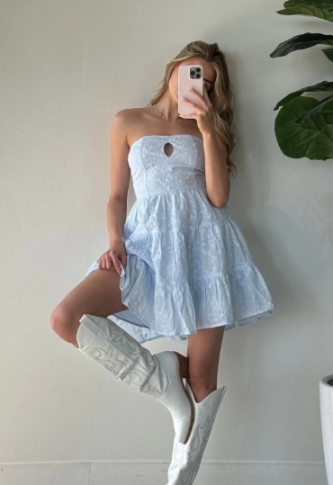 Woman in casual summer dress featuring a strapless pale blue embroidered design with a front cut-out, paired with white cowboy boots.