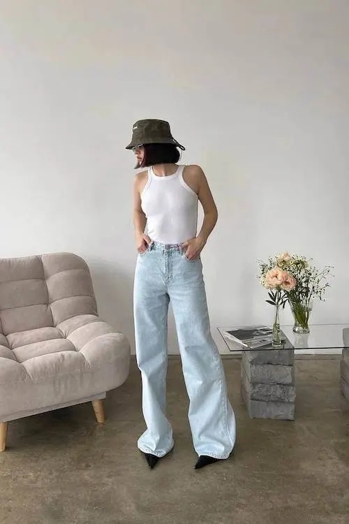 A cute simple outfit styled with a white tank top tucked into high-waisted wide-leg light jeans and a green bucket hat, effortlessly trendy and relaxed.