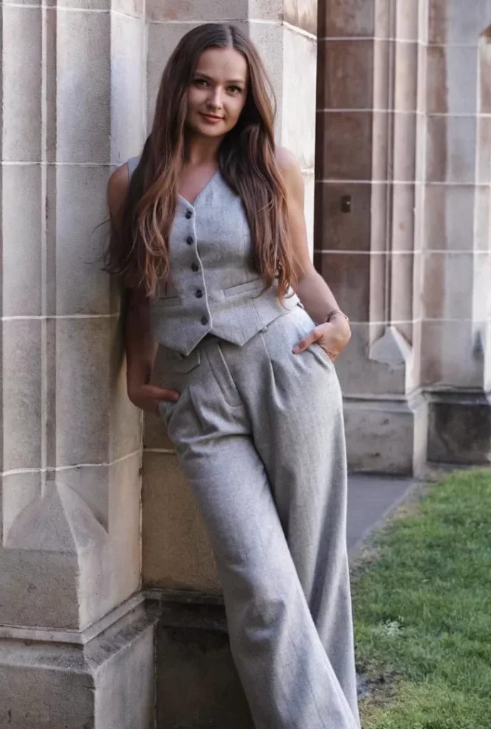 Coordinated grey trouser outfit with a matching tailored vest, styled casually with loose waves, worn leaning against a stone building.