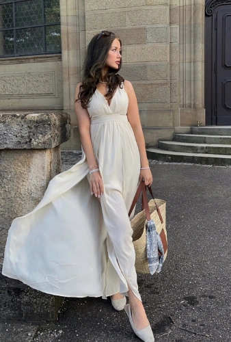 Woman wearing casual summer dress in cream chiffon with a deep V-neckline and high slit, paired with beige flats and a large straw tote bag outdoors.