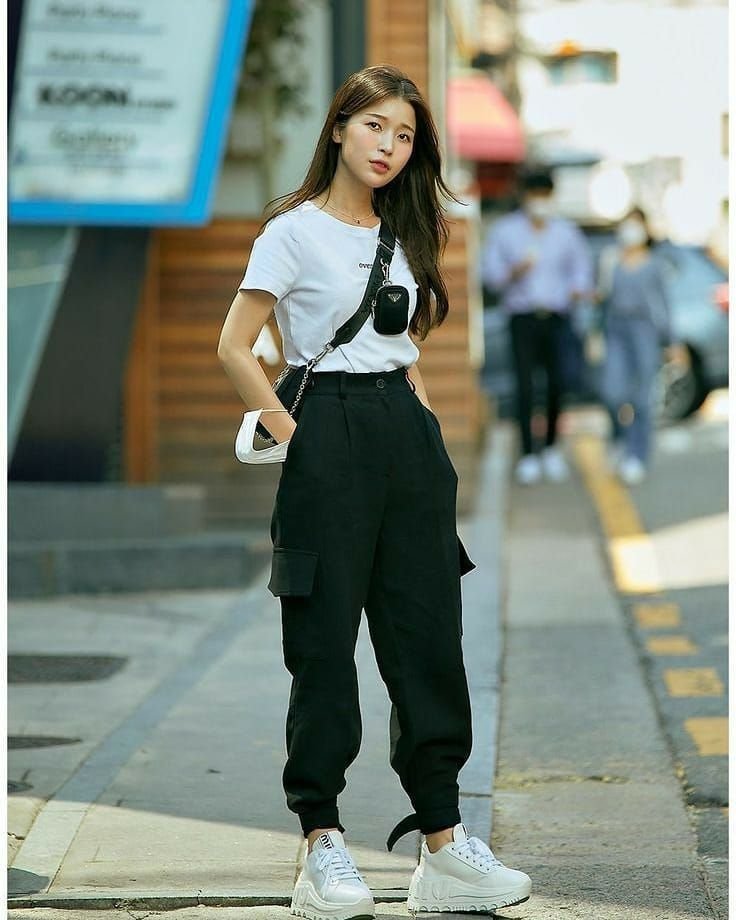 Woman in outfit korean style featuring a white t-shirt, black cargo pants, chunky white sneakers, and crossbody bags on the street.