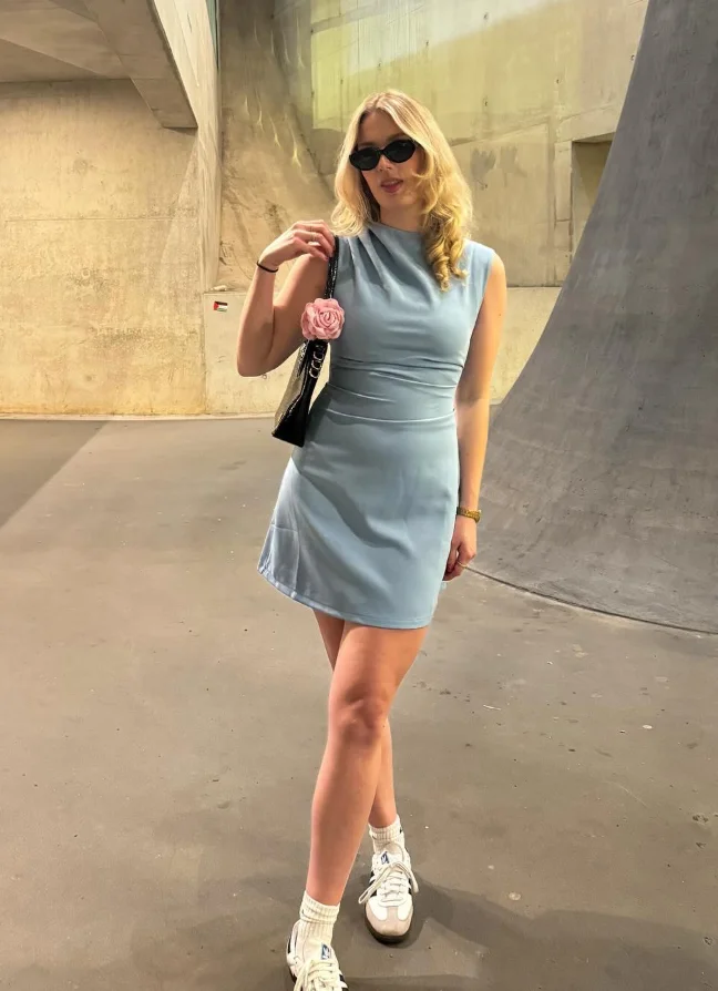 A woman posing indoors in a sleeveless light blue mini dress with retro sneakers and sunglasses, showcasing a minimal yet cute simple outfit.