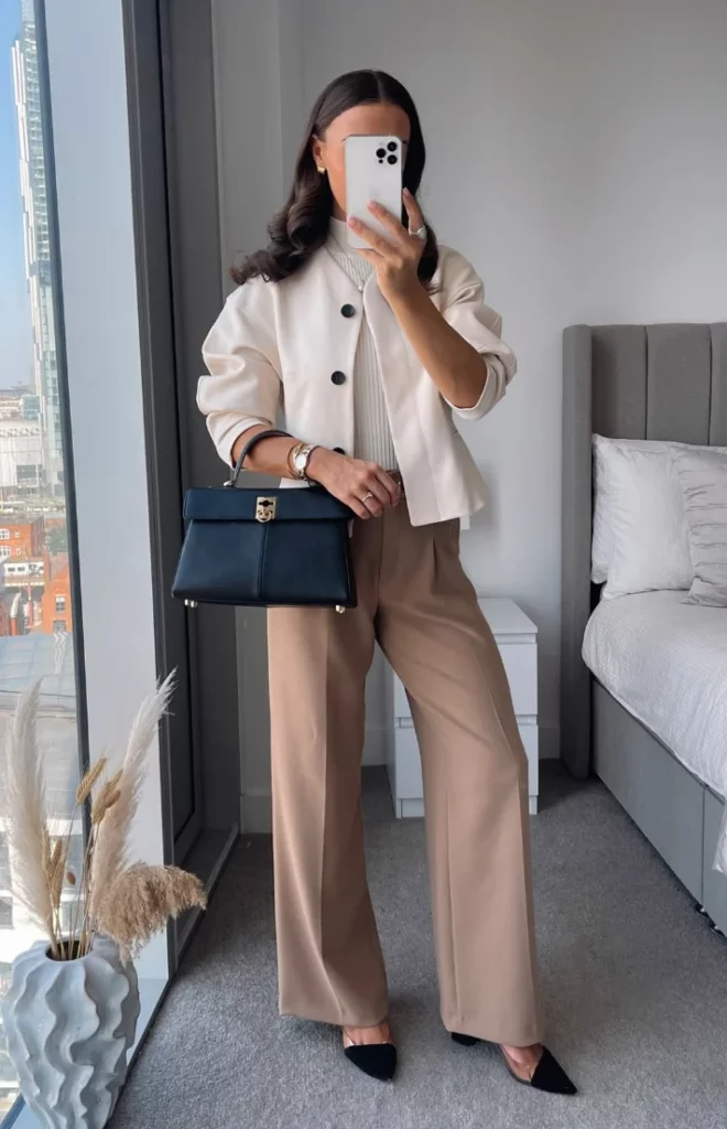 Office outfit with a cream cropped jacket over a white ribbed top, paired with camel wide-leg trousers, black pointed-toe heels, and a structured black handbag for a polished city look.