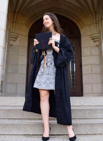 Graduation outfit ideas – black and white lace dress under a classic black graduation gown, paired with black heels and a beaming smile on the steps of a historic building.
