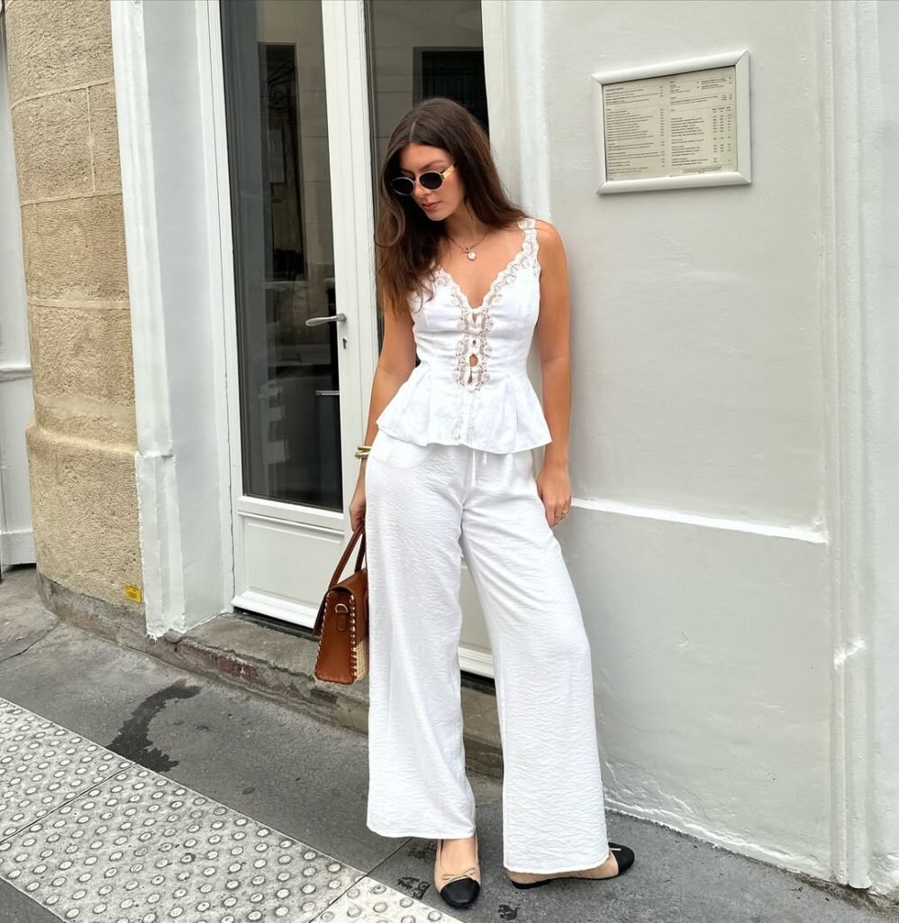 Elegant White Pants Outfits with a white lace-trim corset top and wide-leg white pants, paired with black-and-beige flats and a brown handbag.
