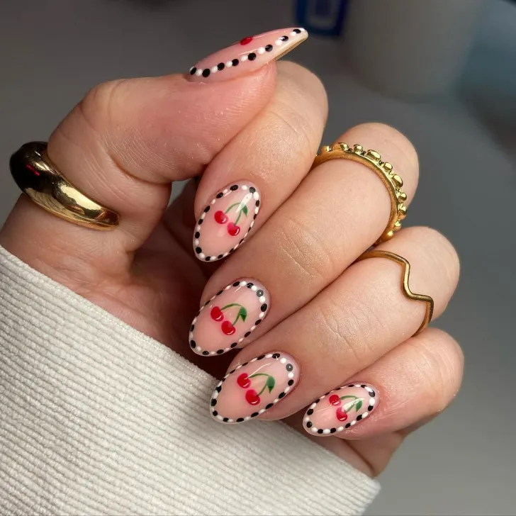 Oval nude nails with black dotted borders framing cute cherry nail art.