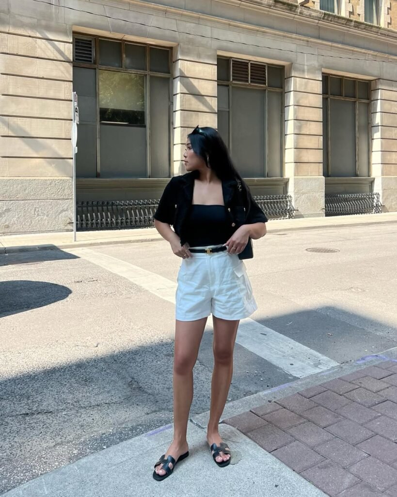 Minimalist Cargo Shorts Outfit with crisp white shorts, a black strapless top, and a cropped jacket, accessorized with a belt and black slide sandals.