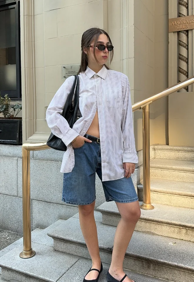 Early Fall Outfit mixing casual and tailored – oversized striped shirt with long denim Bermuda shorts and black Mary Jane flats for a relaxed city look.