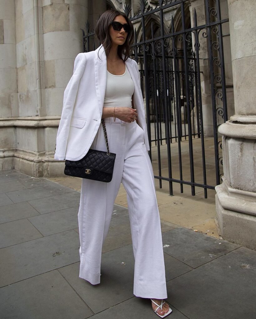 Chic White Pants Outfits with a white tailored blazer, matching wide-leg pants, and a fitted top, styled with a black quilted Chanel bag and white heeled sandals.