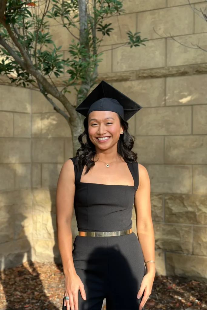 Graduation outfit ideas – sleek black sleeveless jumpsuit with a gold belt, styled with a graduation cap and minimal jewelry for a modern, sophisticated look.