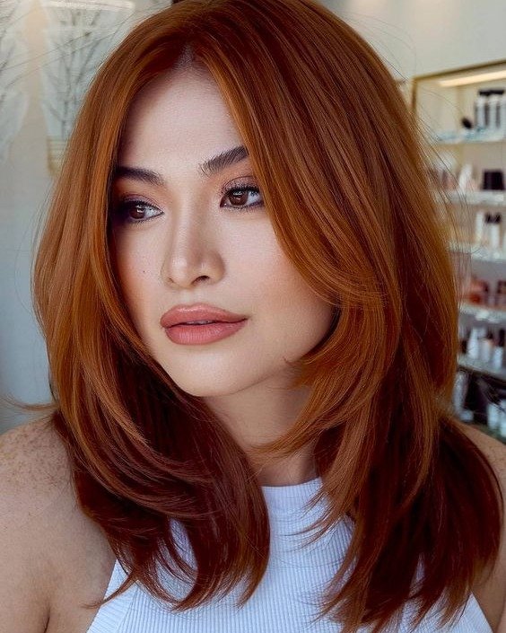 Hairstyles for Medium Length Hair in a rich auburn shade with bold curtain bangs and smooth layers for a glamorous finish.