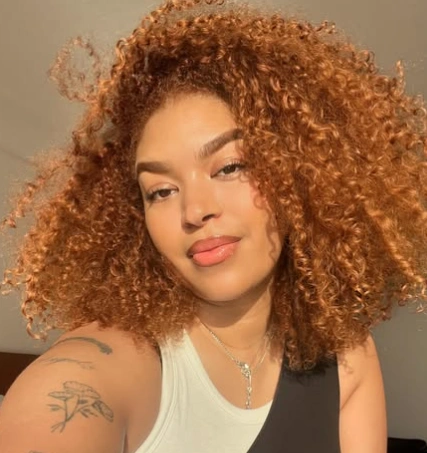 Hairstyles for Medium Length Hair with tight natural curls and warm honey tones, showcasing volume and texture in a bold curly style.