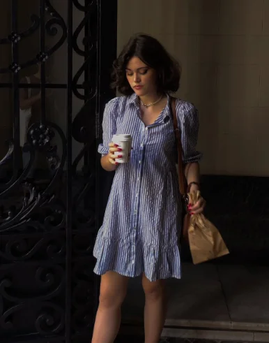 European Summer Outfit: Blue and white striped button-down mini dress with puff sleeves, paired with a brown shoulder bag, holding a coffee cup.