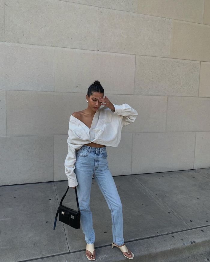 Spring Outfit Ideas with a cropped off-shoulder blouse and high-waisted light-wash jeans, styled with a mini black handbag and heeled sandals.