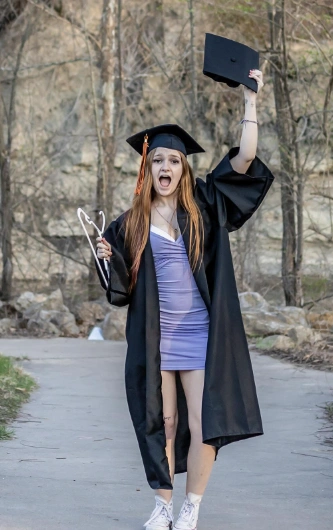 Graduation outfit ideas – light purple bodycon mini dress under a black gown, styled with sneakers, graduation cap, and a stethoscope for a fun, energetic look.