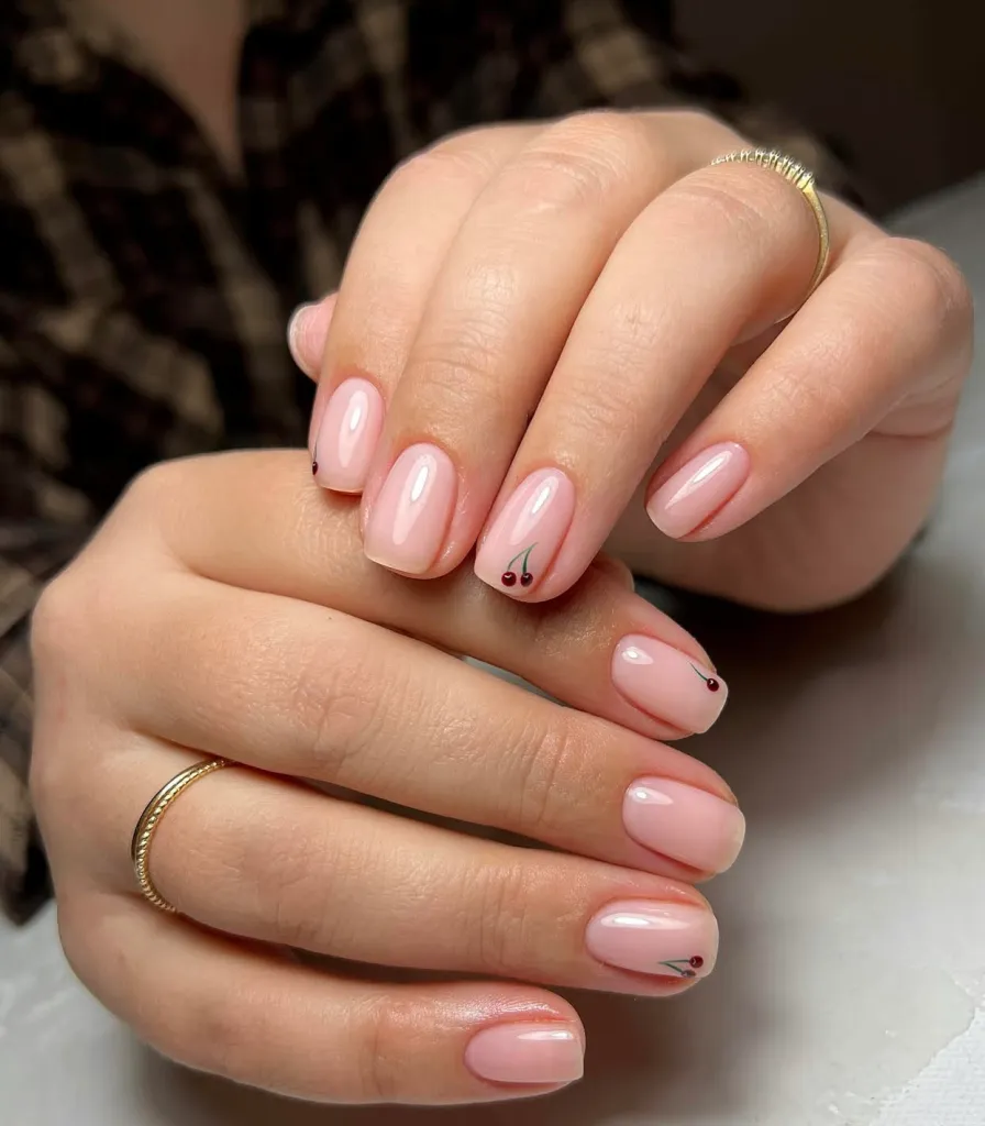 Short nude nails with subtle small cherry nail art on select fingers.