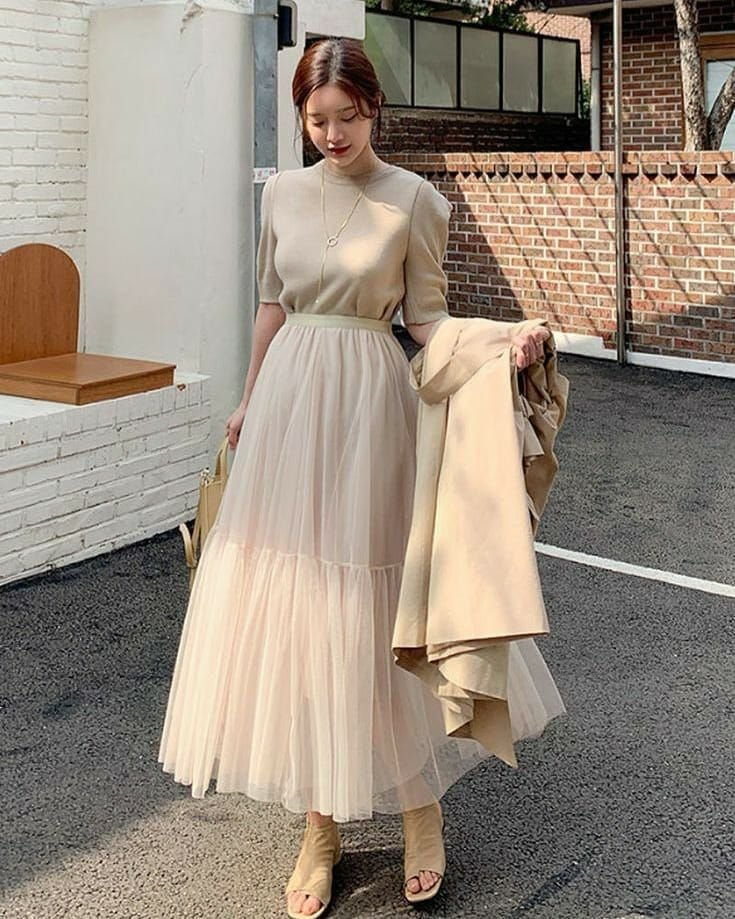 Woman in outfit korean style with a beige short-sleeve top, layered tulle maxi skirt, and beige heeled sandals.