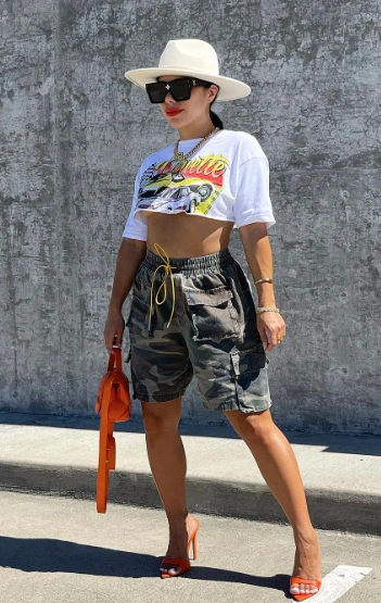Bold summer Cargo Shorts Outfit with camo-print shorts, a white graphic crop top, orange heels, and oversized accessories for a street glam look.