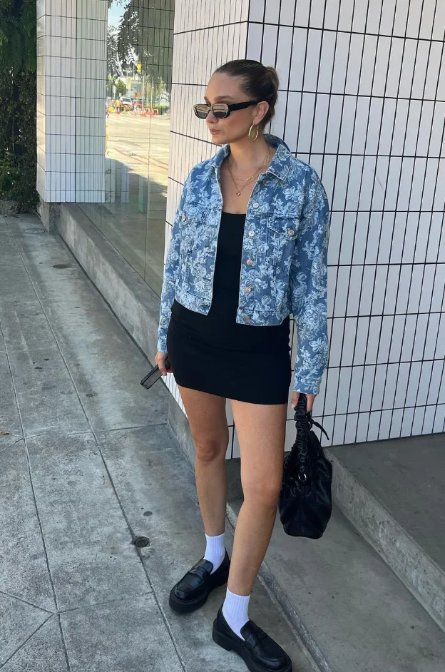 Early Fall Outfit featuring a black mini dress and a floral denim cropped jacket, styled with loafers and white socks – an edgy and fresh transitional look.