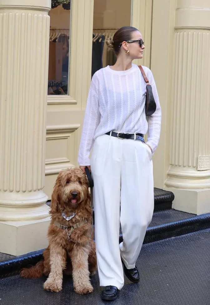 Relaxed White Pants Outfits with a sheer white knit sweater, high-waisted pleated white trousers, black loafers, and a black belt, with a large brown dog sitting beside.