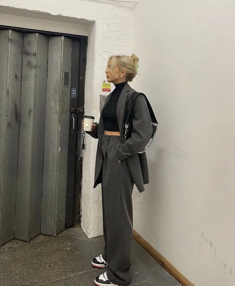 Monochrome grey trouser outfit featuring a cropped black turtleneck, oversized grey blazer, black-and-white sneakers, and chain strap bag.