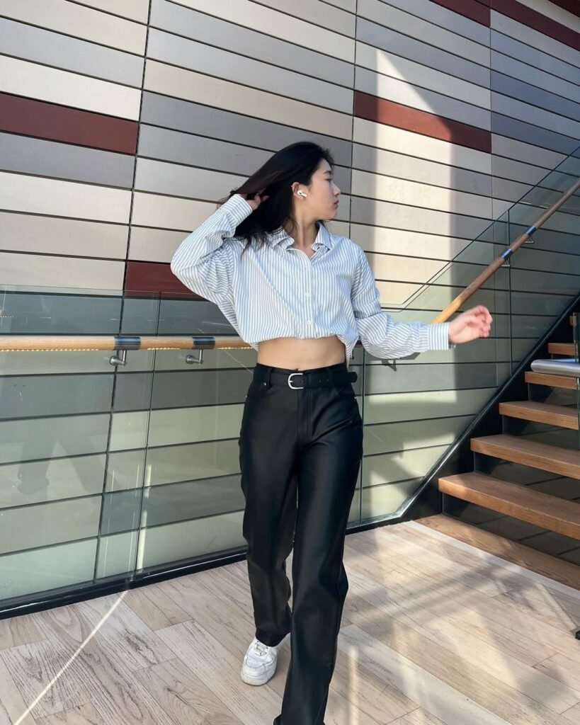 Woman in outfit korean style wearing a cropped striped shirt, black high-waisted pants, and white sneakers indoors.