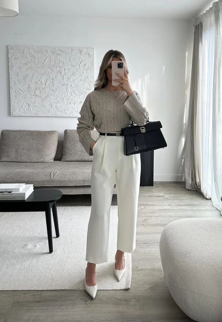 Office outfit in light tones – beige cable-knit sweater tucked into cropped white tailored trousers, styled with white pointed-toe heels and a structured black handbag.