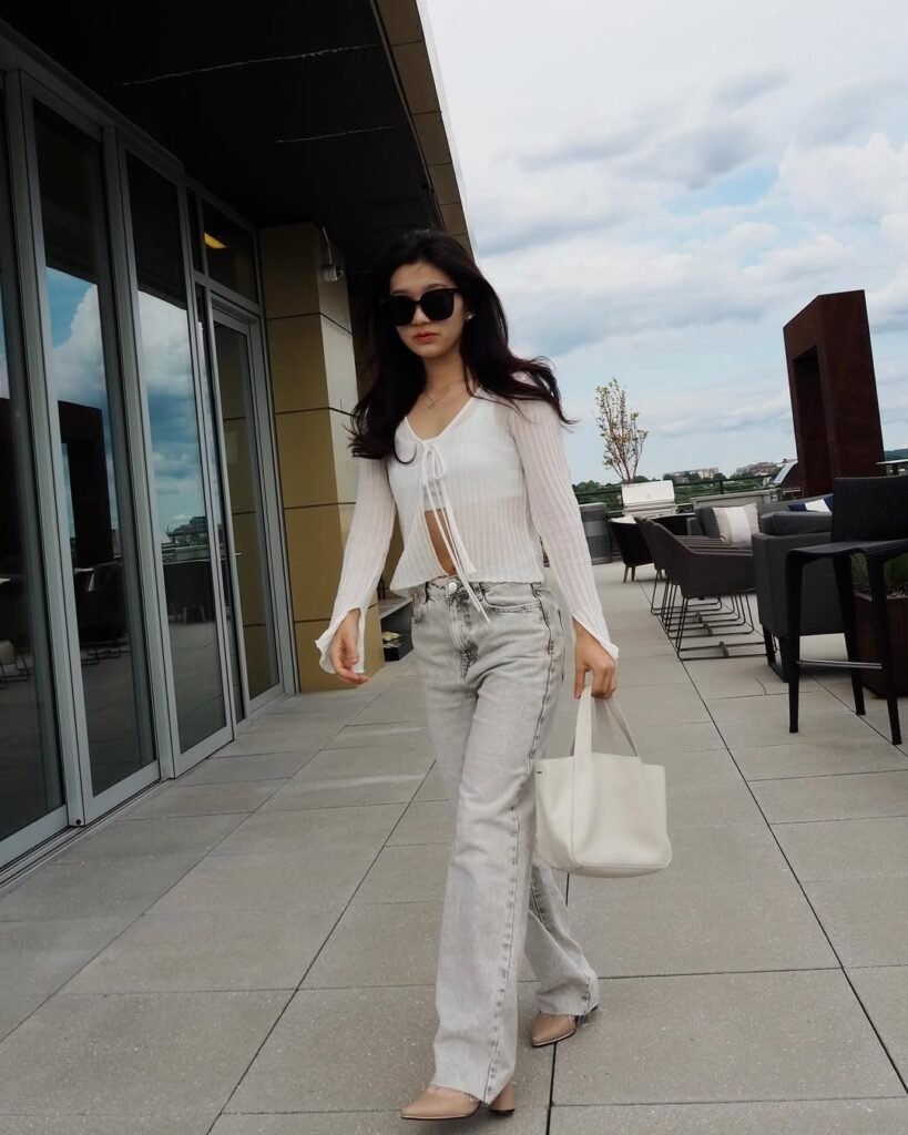 Woman in outfit korean style featuring a white cropped tie-front cardigan, light grey jeans, and beige pointed heels.