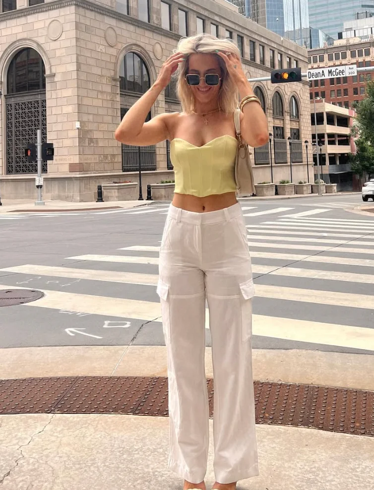 Trendy White Pants Outfits featuring a strapless yellow corset top with white cargo-style trousers, accessorized with sunglasses and gold jewelry.