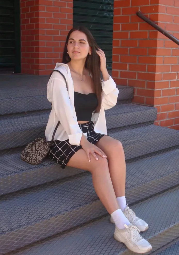 A woman sitting on stairs in a monochrome outfit: black tube top, white shirt, and checkered skirt, styled with white sneakers – a city-ready version of cute simple outfits.