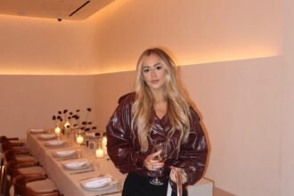 Woman in a burgundy leather jacket, black shorts, and sheer tights holding a glass of wine — an elegant Night Out Outfit for dinner.