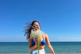 Woman posing on a sunny beach wearing a vibrant blue bikini top, white wrap skirt, and sneakers — a fun and stylish example of beach outfit ideas.