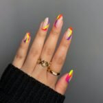 Hand with almond-shaped summer nails featuring neon orange, yellow, pink, and purple abstract swirls on a nude base — a bold and trendy summer nails design.