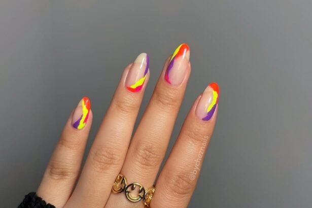 Hand with almond-shaped summer nails featuring neon orange, yellow, pink, and purple abstract swirls on a nude base — a bold and trendy summer nails design.