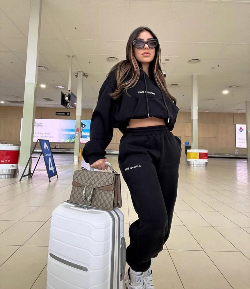 Fashionable traveler in all-black sweatsuit and designer bag walking confidently – classic all-black airport outfit.