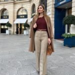 Woman in a maroon top and beige wide-leg trousers, layered with a camel coat – an elegant outfit suited for fall street style.