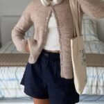 Casual cardigan outfit with a light brown fuzzy cardigan and navy shorts, accessorized with headphones and a tote bag.