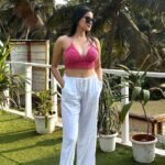 A woman wearing a pink crochet halter top paired with white linen pants, sunglasses, and relaxed posture, enjoying a warm afternoon, ideal for a chic brunch in a tropical setting.