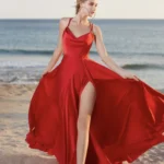A woman in a satin red dress with a thigh-high slit, twirling on the beach, her dress flowing in the wind.