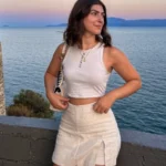 Casual summer look with a white tank top and linen mini skirt, styled with natural makeup and ocean sunset in the background — perfect for relaxed outfit ideas summer.