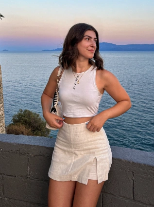 Casual summer look with a white tank top and linen mini skirt, styled with natural makeup and ocean sunset in the background — perfect for relaxed outfit ideas summer.