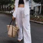 Woman dressed in white ribbed sleeveless top with beige linen pants, carrying a large brown handbag.