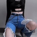 Grunge Outfits: Person with long red hair wearing a black lace-up halter crop top, black flared pants, and platform shoes standing on a city street.