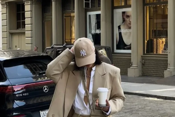 Woman in a camel oversized blazer over white shirt and tan wide-leg pants, accessorized with a tan cap and coffee cup, walking on a city street. Blazer Outfits.
