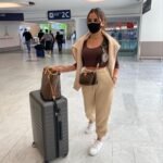 Cute Airport Outfits: Woman in beige joggers and a brown top with a Louis Vuitton crossbody bag, pulling a grey suitcase at Terminal 2C.