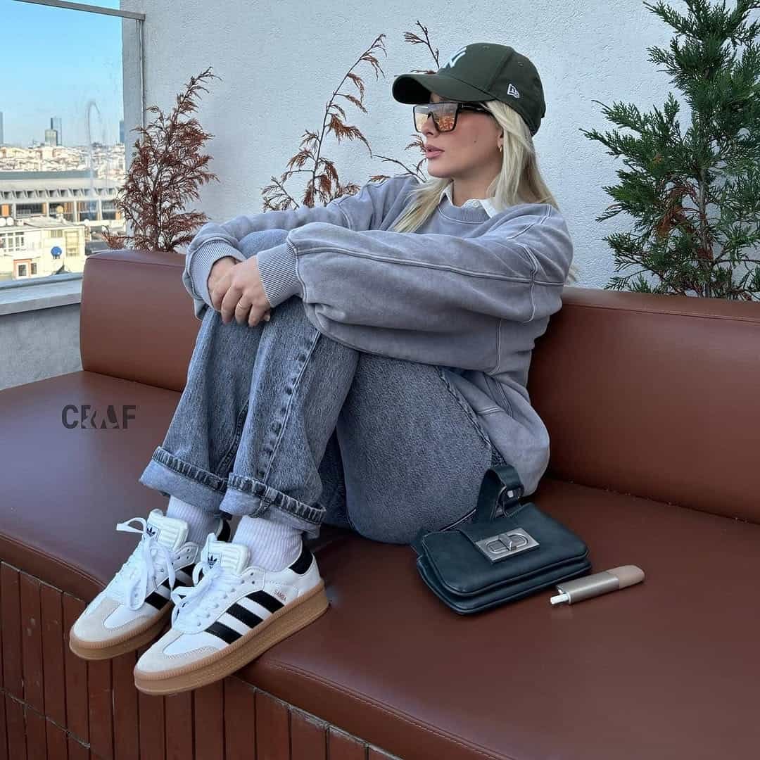 Casual rooftop look featuring Adidas Samba Outfits with a grey oversized sweatshirt, cuffed jeans, and dark green cap.