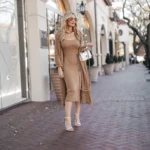 Elegant woman in a camel knit dress and long cardigan, paired with strappy heels and a silver designer bag — look expensive outfits.