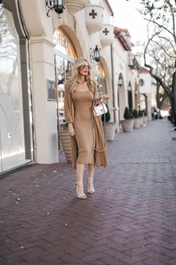 Elegant woman in a camel knit dress and long cardigan, paired with strappy heels and a silver designer bag — look expensive outfits.